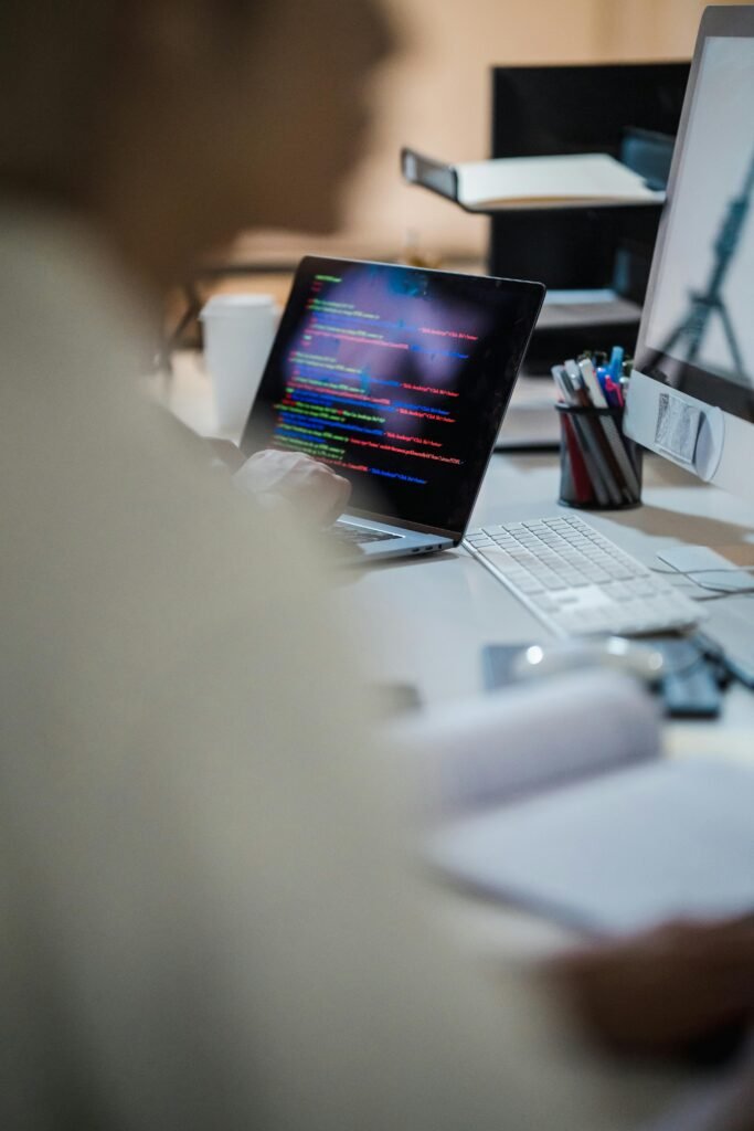Blurred figure at a desk with a laptop displaying colorful code, indicating a programming environment.