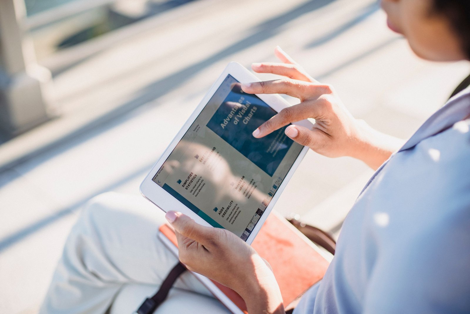 A woman using a tablet outside, browsing in natural light.